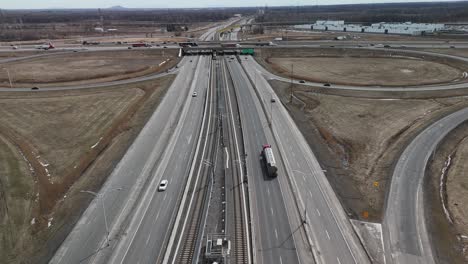 The-Réseau-express-métropolitain-REM-automated-light-rail-system-in-Brossard,-near-Montreal-city-driving-on-main-highway-with-traffic-car-and-truck,-aerial-drone-footage