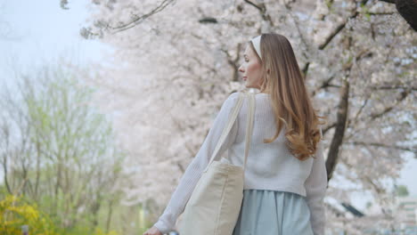 Caucasian-Woman-With-Tote-Bag-Walking-Under-The-Sakura-Trees-In-Bloom-In-Yangjae-Citizens-Forest-In-Seocho,-Seoul,-South-Korea