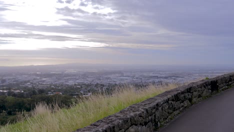 Panorama-De-La-Ciudad-De-Auckland-Visto-Desde-El-Camino-Hasta-La-Cima-De-Una-Colina-De-árboles-Que-Se-Convierte-En-Una-Carretera-Asfaltada-De-Montaña