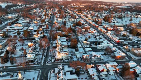 Wide-aerial-reveal-of-snowy-American-town-during-golden-hour-winter-sunset