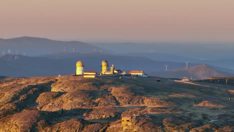 Teleaufnahme-Einer-Alten-Verlassenen-Radarstation-Mit-Windturbinen-Im-Hintergrund-Auf-Dem-Gipfel-Des-Naturparks-Serra-Da-Estrela,-Portugal