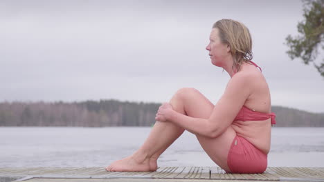 Sorrowful-mature-woman-in-swimwear-sits-on-pontoon-after-cold-water-immersion