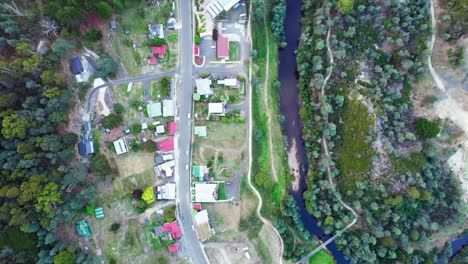 Vista-Aérea-De-Arriba-Hacia-Abajo-De-Una-Pequeña-Ciudad-A-Lo-Largo-Del-Estrecho-Río-Derby,-Tasmania