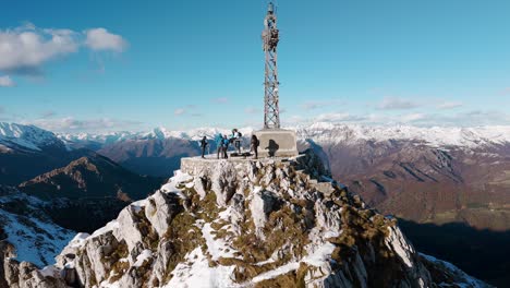 Reverse-aerial-group-of-climbers-at-peak-of-rugged-snowy-peak-in-Italy-alps