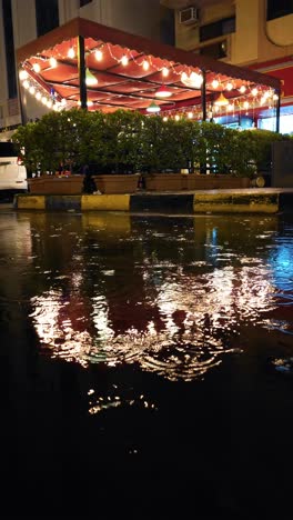 En-Una-Noche-Lluviosa,-Las-Luces-Del-Restaurante-Se-Reflejan-En-El-Agua-De-Lluvia,-Creando-Una-Escena-Fascinante.