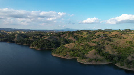 Establishing-drone-shot-of-lake-and-green-hilly-landscape-of-Dominican-Republic-at-sunset-time