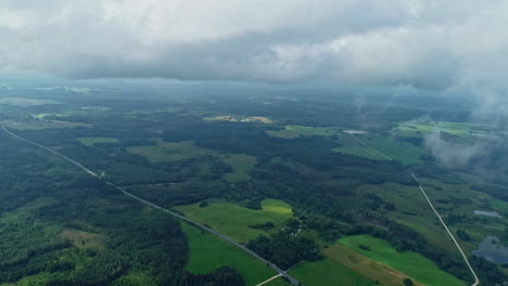 Wet-green-cloudy-skyline-above-rural-fields-flying-drone-perspective-airplane-view,-countryside-meadow-between-trees-forest,-horizon-background-at-daylight