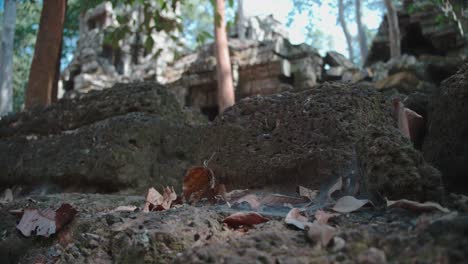 Die-Alten-Ruinen-Von-Angkor-Wat-Ragen-über-Einen-Steinigen-Vordergrund,-Der-Mit-Trockenen-Blättern-übersät-Ist