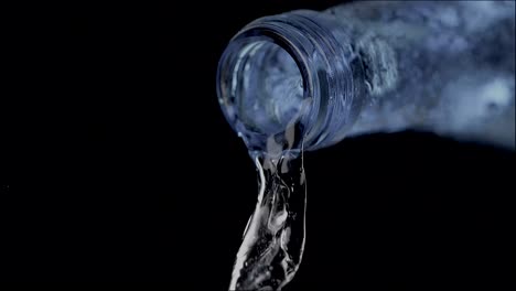 Vista-De-Cerca-De-Un-Hilo-De-Agua-Con-Gas-En-Cámara-Lenta-Que-Fluye-Desde-El-Cuello-De-Botella-De-Un-Vaso,-Proyectando-Un-Reflejo-Azul-Sobre-El-Fondo-Negro,-Simbolizando-El-Concepto-De-Pureza-Y-Refresco