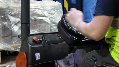 worker-wearing-yellow-protective-shirt,-caucasian-labor-starting-the-electric-forklift-and-drive-inside-industrial-warehouse-shipping-packaging