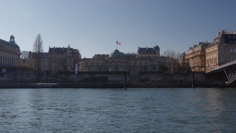 People-walking-by-the-Seine-River-on-a-sunny-day,-beautiful-Paris-cityscape