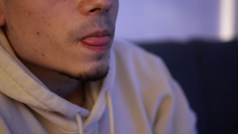 Close-up-shot-of-a-young-man-sitting-on-the-couch-and-vaping-from-a-blue-tobacco-heating-device