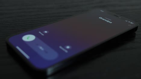 Close-up-shot-of-an-iPhone-receiving-a-call-from-Grandpa-on-black-wooden-table