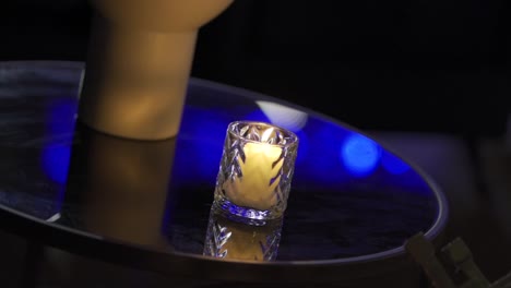 Candle-in-glass-container-lit-on-glass-table-in-party-decoration