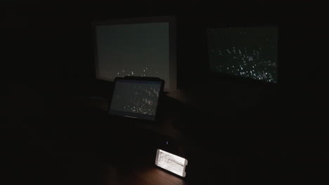 A-side-angle-shot-of-four-digital-computer-device-screens-flashing-a-strobing-static-noise-pattern-in-a-dark-room