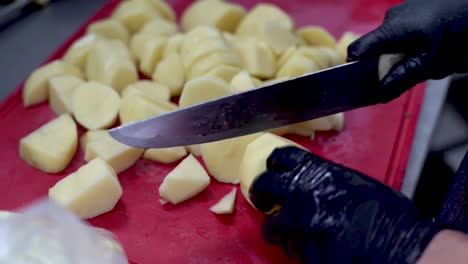 Manos-Del-Chef-Dividiendo-Patatas-Peladas-Crudas-En-Una-Tabla-De-Cortar-Roja,-De-Cerca