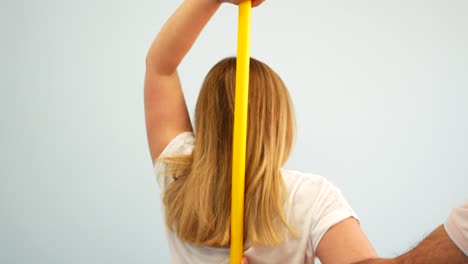 Blonde-woman-doing-shoulder-mobility-exercise-with-stick-supervised-by-physiotherapist