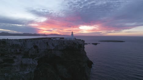 Fire-Sunset-skyline-aerial-drone-zooms-Cavalleria-lighthouse-cliff,-north-of-Menorca-architecture-at-ocean-edge