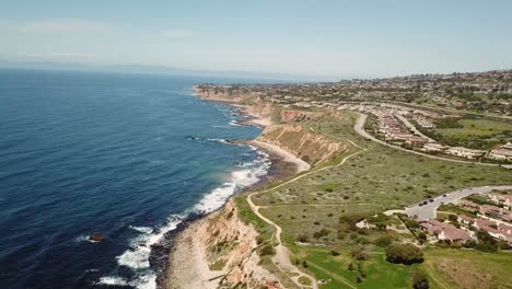 4K-Aerial-View-of-the-Pacific-Ocean-with-Cliffs-in-Palos-Verdes,-Los-Angeles,-California-on-a-Warm,-Sunny-day-with-Mountains-in-the-Background
