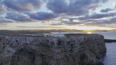 Luftaufnahme-Des-Leuchtturms-Von-Cavalleria,-Menorca,-Meeresklippe,-Sonnenuntergang,-Skyline-Hintergrund,-Spanisches-Naturziel