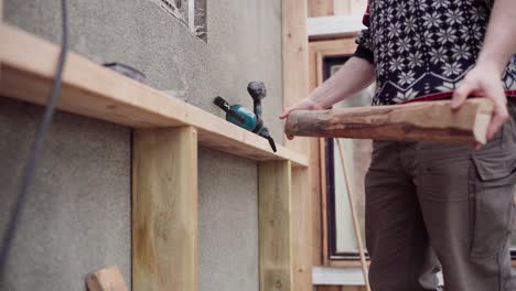 Man-With-Cordless-Driller-Screwing-Piece-Of-Wood-On-Brace