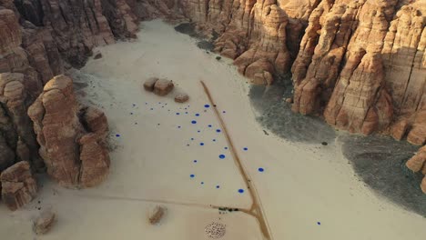 Aerial-view-a-blue-dot-artwork-in-middle-of-sandstone-mountains-at-Desert-X-AlUla,-Saudi-Arabia