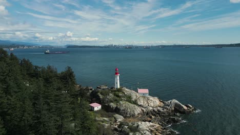 aerial-view-tilting-down-point-atkinson-lighthouse-in-lighthouse-park-near-vancouver-city-on-an-sunny-day-with-some-clouds-in-British-Columbia,-Canada
