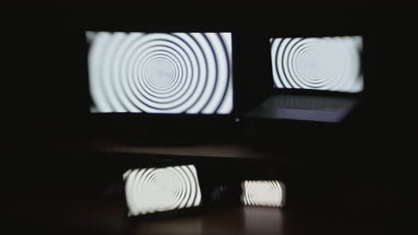 Front-angle-shot-of-a-hypnotic-spiral-pattern-displayed-on-four-device-screens-in-a-dark-room-with-selective-focus-and-a-choppy-shutter-speed-effect