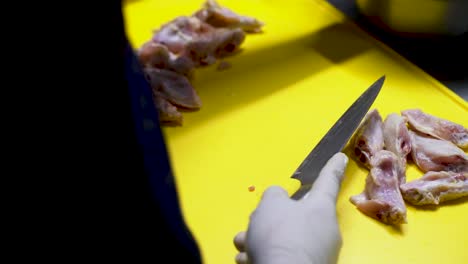 Chef-wearing-sterilized-white-gloves-slicing-chicken-wings-with-a-sharp-knife-on-a-yellow-cutting-board-for-a-milanesas-recipe