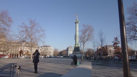 Person-And-Dog-Walking-In-The-Street-With-July-Column-At-Place-de-la-Bastille-In-Paris,-France