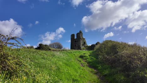 Rural-scene-path-to-historic-Dunhill-medieval-castle-on-a-beautiful-spring-day-with-blue-sky-skies-and-bright-clouds-moving-by-landscape-scene-in-Waterford-Ireland