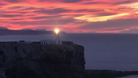 Sunset-aerial-shining-lighthouse-Cavalleria,-Menorca-Spanish-cliff-ocean-coastline-panoramic-gradient-golden-hour-skyline