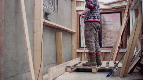 Man-Measuring-The-Height-Of-Wooden-Brace-For-Shelf-Inside-The-Greenhouse