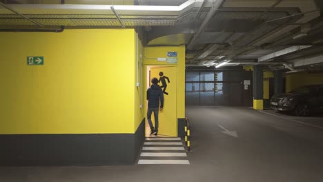 Back-view-of-young-man-opening-emergency-door-exit-in-underground-parking-lot-garage