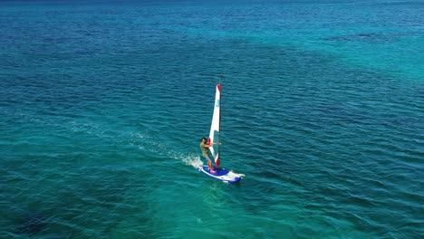 Aerial-view-following-a-person-windsurfing-in-Costa-Smeralda,-Sardinia---circling,-drone-shot