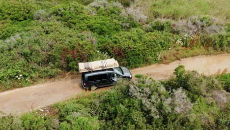 Aerial-view-around-a-car-driving-on-a-dirt-road-in-sunny-Sardinia,-Italy---circling,-drone-shot