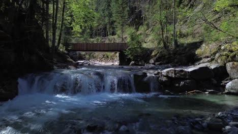 Drohnen-Neigungsflug-über-Einem-Wunderschönen-Gebirgsfluss-In-Richtung-Einer-Von-Wäldern-Umgebenen-Brücke