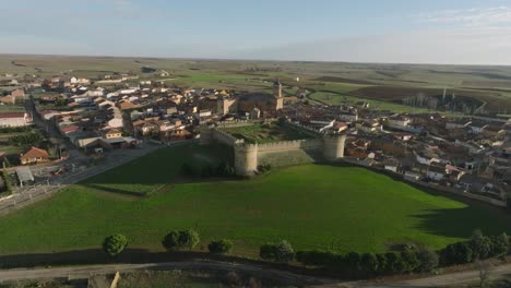 Castle-with-towers-along-rural-meadow-village-aerial-drone-at-Grajal-de-Campos-town,-Spain