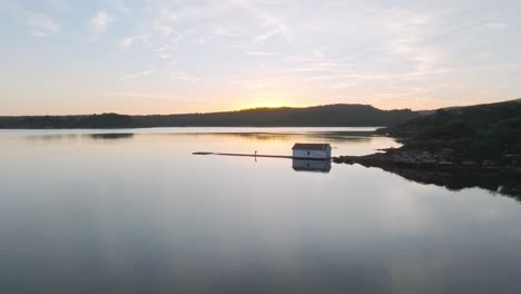 Drones-Vuelan-Bajo-Sobre-El-Agua-Reflejada-De-La-Bahía-De-Fornells-En-Menorca-España-Destino-Costero-De-Viaje,-Fondo-Del-Horizonte-Colorido-Del-Atardecer,-Vista-Aérea