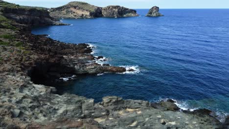 Aerial-view-tilting-over-people-enjoying-the-day-on-the-rocky-coast-of-Pantelleria,-Sicily,-Italy