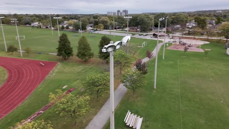 Drohnenaufnahme,-Die-Tagsüber-Um-Einen-Großen-Sportplatz-Mit-Licht-Kreist,-Mit-High-School-Laufbahn-Im-Hintergrund