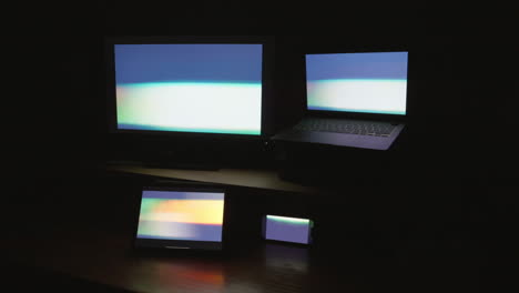 Four-digital-computer-device-screens-displaying-a-strobing-pattern-in-a-dark-room