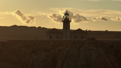 Sunset-skyline-lighthouse-above-mediterranean-cliff-landscape-aerial-drone-Punta-Nati-Menorca-Spain-orbit,-golden-background