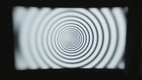 Head-on-shot-of-a-single-computer-screen-with-a-hypnotic-spiral-pattern-displayed-in-a-dark-room-with-selective-focus-and-a-choppy-shutter-speed-effect