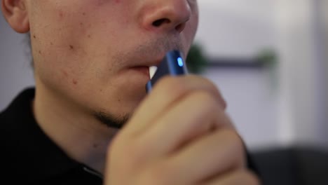 Close-up-shot-of-a-young-man-using-a-tobacco-heating-device-in-the-house