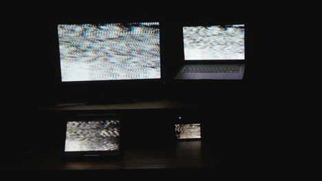 Four-digital-computer-device-screens-flashing-a-strobing-static-noise-pattern-in-a-dark-room
