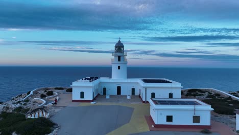 Aerial-drone-zooms-in-Cavalleria-lighthouse-architectural-tower-marine-seascape,-sunset-skyline-at-north-of-Menorca-Europe-Spain