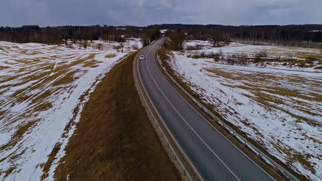 Weißes-Fahrzeug-Fährt-Asphaltstraße-Mit-Schneebedeckten-Feldern,-Luftdrohnenansicht