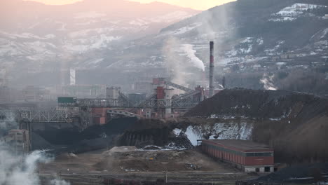 La-Tarde-Desciende-Sobre-Un-Complejo-Industrial-En-Medio-De-Un-Paisaje-Montañoso,-Con-El-Humo-De-Una-Chimenea-Difundiéndose-Suavemente-Hacia-El-Cielo.