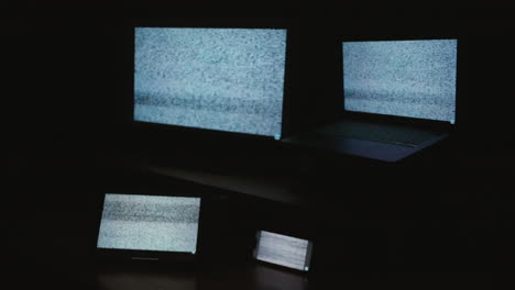 A-side-angle-shot-of-four-digital-computer-device-screens-displaying-a-choppy-static-noise-pattern-in-a-dark-room
